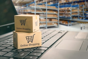 Online shopping / ecommerce and delivery service concept : Paper cartons with a shopping cart or trolley logo on a laptop keyboard, depicts customers order things from retailer sites via the internet.